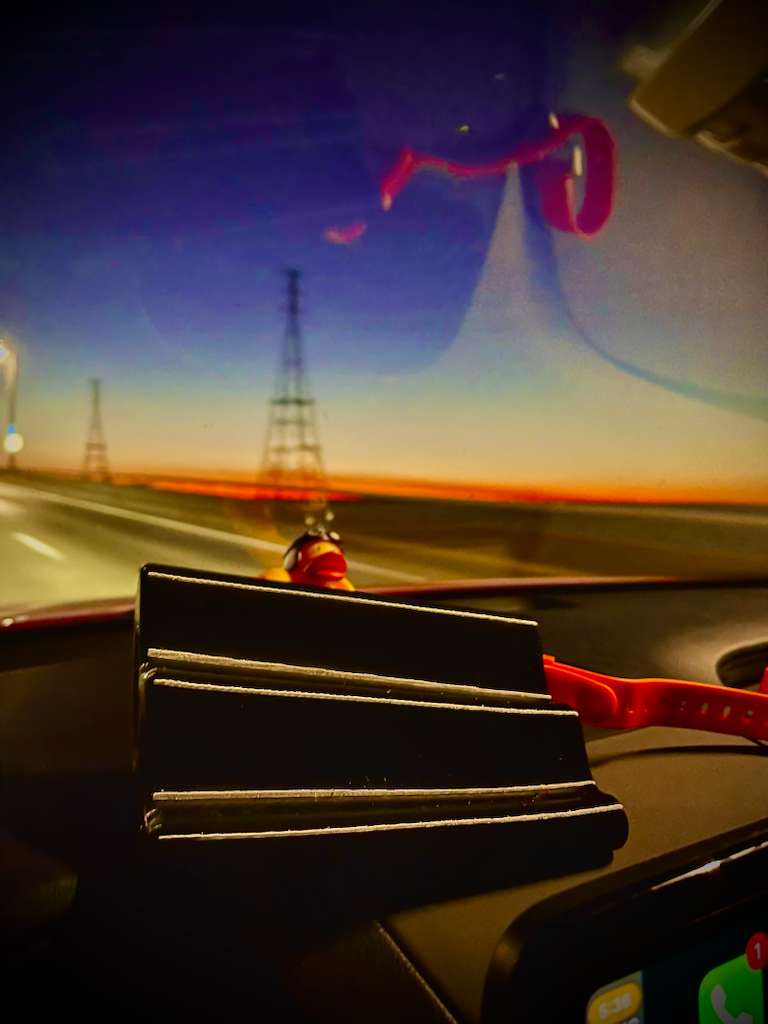 Prototype PillowFlow cushion resting on a car dashboard during sunset, with blurred highway towers and warm sky colors in the background.